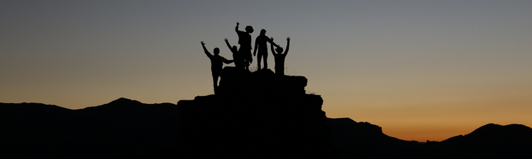 silhouette of people standing on hilltop at sunset
